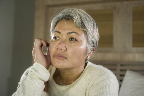 dramatic lifestyle home portrait of attractive sad and depressed middle aged woman with grey hair on bed feeling upset suffering depression and anxiety