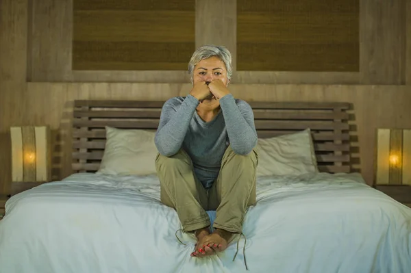 Dramatisches Lebensstil-Porträt einer attraktiven, traurigen und verlorenen Frau mittleren Alters mit grauen Haaren, die frustriert auf dem Bett sitzt und unter Depressionen und Schmerzen leidet — Stockfoto