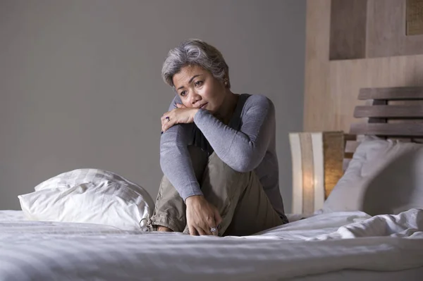 Dramatisches Lebensstil-Porträt einer attraktiven, traurigen und verlorenen Frau mittleren Alters mit grauen Haaren, die frustriert auf dem Bett sitzt und unter Depressionen und Schmerzen leidet — Stockfoto