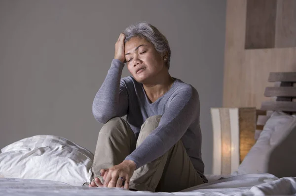 Dramatisches Lebensstil-Porträt einer attraktiven, traurigen und verlorenen Frau mittleren Alters mit grauen Haaren, die frustriert auf dem Bett sitzt und unter Depressionen und Schmerzen leidet — Stockfoto