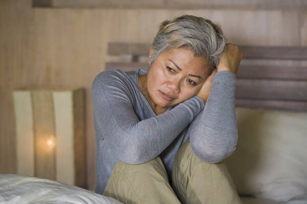 dramatic lifestyle home portrait of attractive sad and lost middle aged woman with grey hair sitting on bed feeling frustrated suffering depression and pain