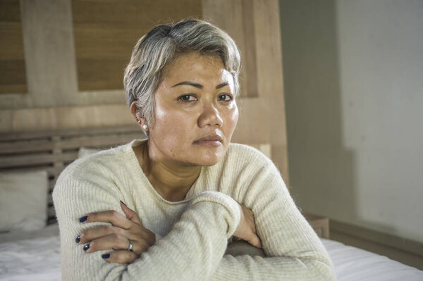 dramatic lifestyle home portrait of attractive sad and lost middle aged woman with grey hair sitting on bed feeling frustrated suffering depression and pain
