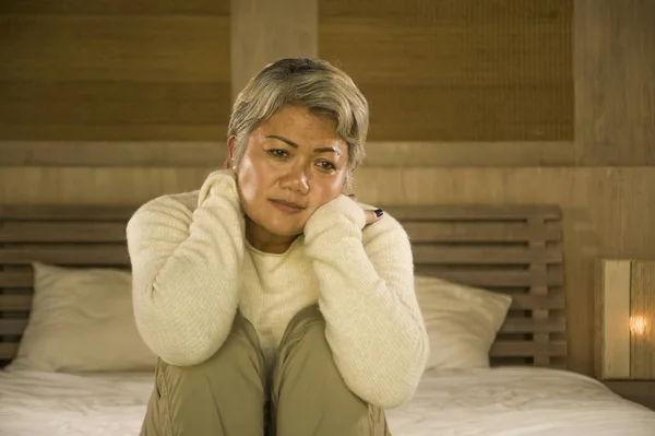 Dramatisches Lebensstil-Porträt einer attraktiven, traurigen und verlorenen Frau mittleren Alters mit grauen Haaren, die frustriert auf dem Bett sitzt und unter Depressionen und Schmerzen leidet — Stockfoto