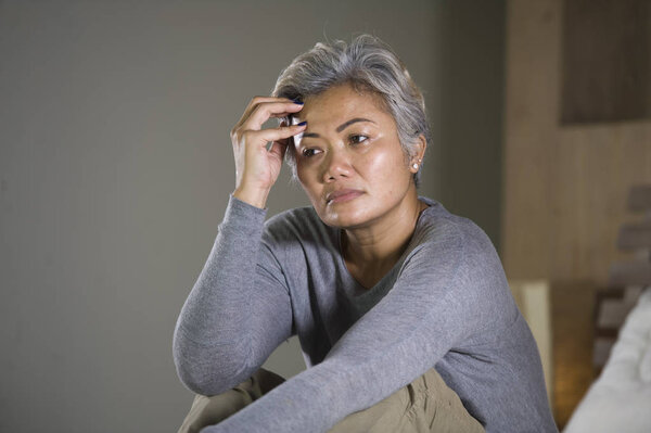 dramatic lifestyle home portrait of attractive sad and lost middle aged woman with grey hair sitting on bed feeling frustrated suffering depression and pain