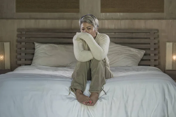 Dramatisches Lebensstil-Porträt einer attraktiven, traurigen und verlorenen Frau mittleren Alters mit grauen Haaren, die frustriert auf dem Bett sitzt und unter Depressionen und Schmerzen leidet — Stockfoto