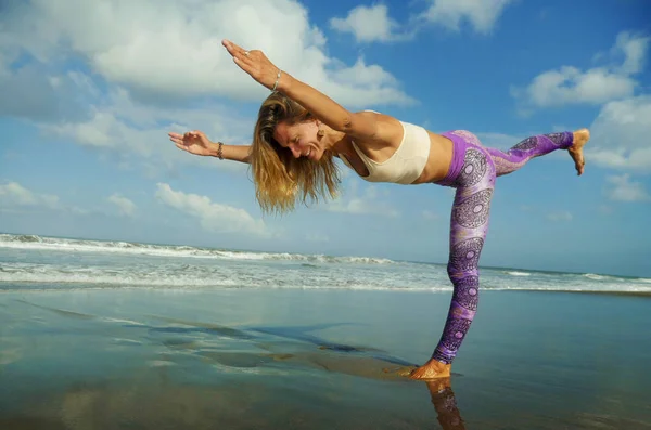 Joven mujer rubia feliz y atractiva haciendo yoga y ejercicio de meditación al aire libre en la hermosa playa en la práctica de relajación y flexibilidad al aire libre en el bienestar y estilo de vida saludable — Foto de Stock