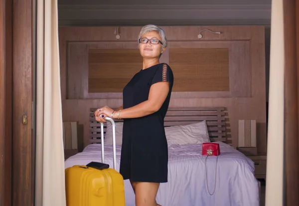attractive and happy middle aged Asian woman in stylish Summer dress arriving to hotel opening room balcony door looking delighted enjoying travel holidays getaway