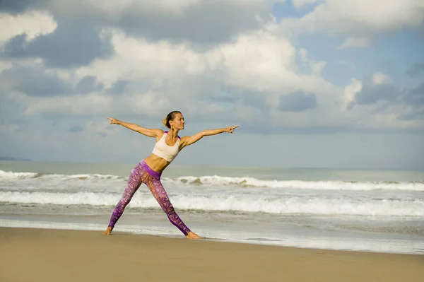 Young happy and attractive woman in yoga pants stretching and doing flexibility and meditation exercise at beautiful beach in wellness and healthy natural lifestyle — Stock Photo, Image
