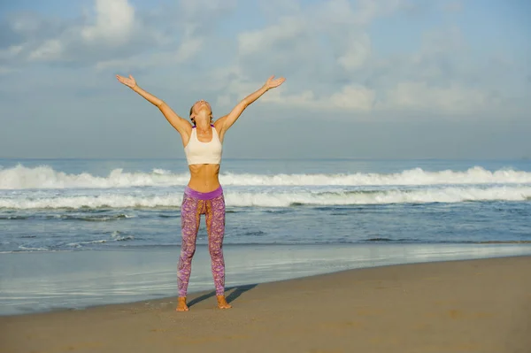 Joven mujer feliz y atractiva en pantalones de yoga estirándose y haciendo ejercicio de flexibilidad y meditación en la hermosa playa en bienestar y estilo de vida natural saludable — Foto de Stock