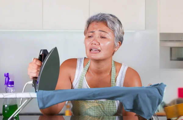 Stressed middle aged Asian woman ironing in stress at home kitchen feeling overwhelmed and tired of working domestic chores in helpless housewife housekeeping — Stock Photo, Image