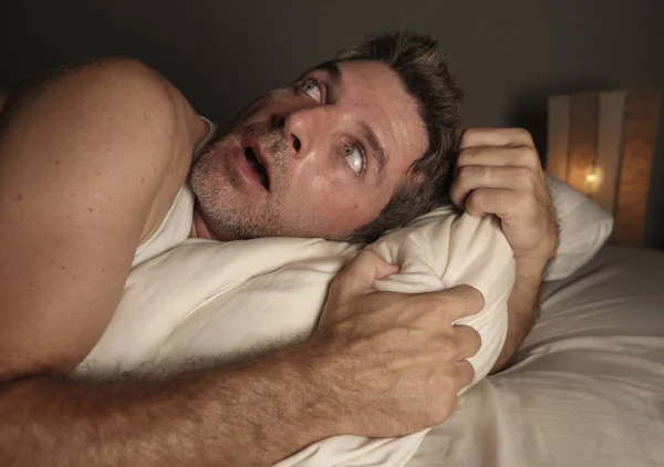 Lifestyle portrait of young attractive scared and paranoid man lying in bed having  bad dreams and nightmares looking around in funny face expression suffering paranoia — Stock Photo, Image