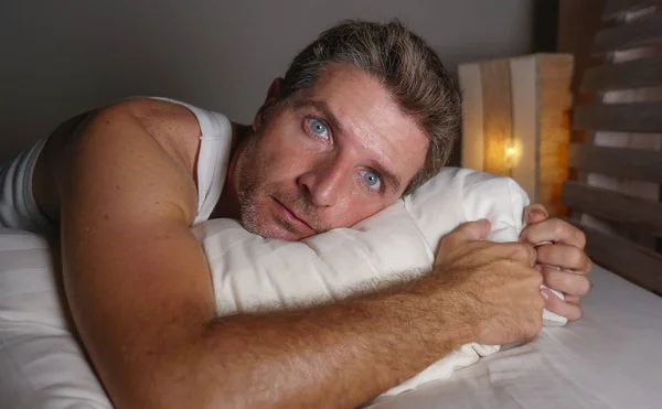close up face portrait of sleepless and awake attractive man with eyes wide open at night lying on bed suffering insomnia sleeping disorder trying to sleep