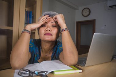 dizüstü bilgisayar masası üzerinde çalışan üzgün ve depresif orta yaşlı çekici Asyalı kadının ofis yaşam tarzı portre stresli ve yorgun duygu boğulmuş