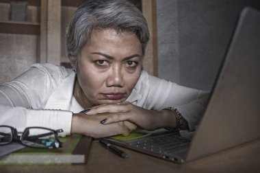 depresif ve overworked orta yaşlı çekici Asyalı kadın dizüstü bilgisayar masasında stres çalışan üzgün duygu ve mutsuz görünümlü boğulmuş