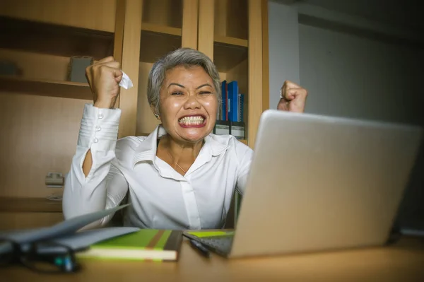 Привлекательная отчаявшаяся и напряженная азиатка средних лет, кричащая жестом, перегруженная работой и работающая за офисным компьютером, чувствует себя эксплуатируемой. — стоковое фото