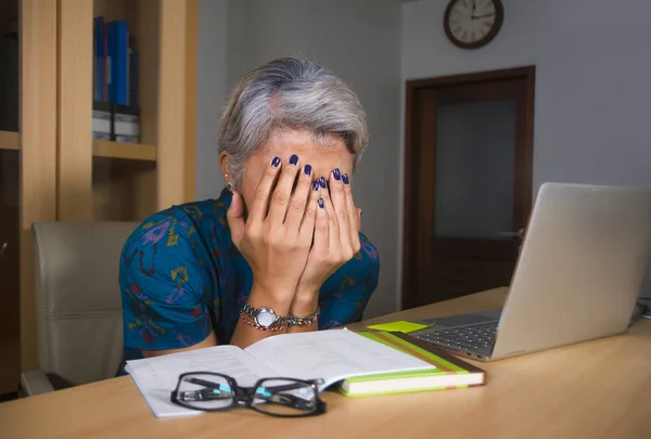 Deprimida e sobrecarregada meia-idade atraente mulher asiática trabalhando em estresse na mesa de computador portátil cobrindo seu rosto chorando oprimido olhando exausto — Fotografia de Stock