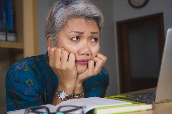 Deprimida e sobrecarregada meia-idade atraente mulher asiática trabalhando em estresse na mesa de computador portátil cobrindo seu rosto chorando oprimido olhando exausto — Fotografia de Stock