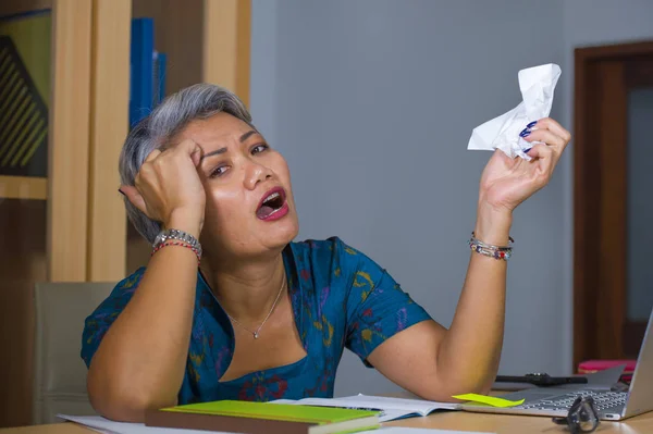 Przygnębiony i przepracowany w średnim wieku atrakcyjny Asian kobieta praca w stres na laptop komputer biurko uczucie zdenerwowany i ogarnia w zdenerwowany twarz wyrażenie — Zdjęcie stockowe