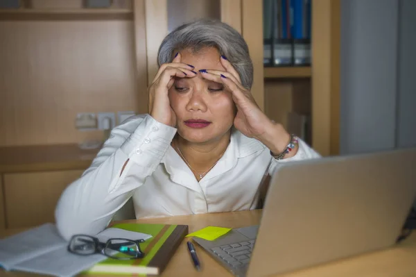 Deprimida e sobrecarregada de meia-idade atraente mulher asiática trabalhando em estresse na mesa do computador portátil sentindo-se chateado e oprimido olhando infeliz — Fotografia de Stock