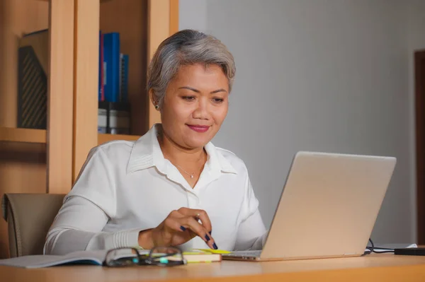 Corporate job lifestyle portrait of happy and successful attractive middle aged Asian woman working at office laptop computer desk satisfied and efficient in business success — Stock Photo, Image