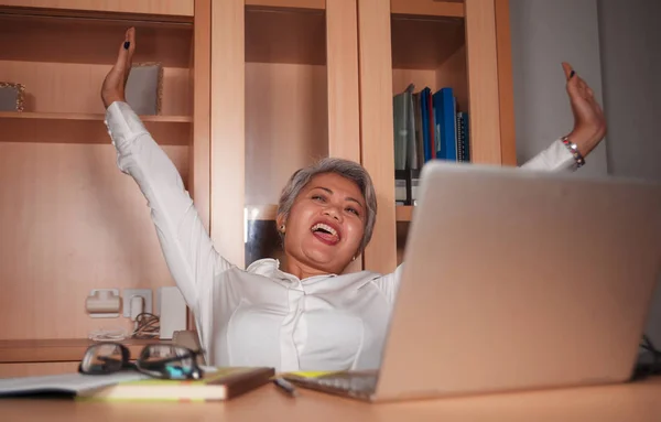 Щасливий і успішний середній у віці Азіатська жінка працює в офісі портативний комп'ютер стіл збуджені і веселий святкування ділової перемоги сміятися — стокове фото