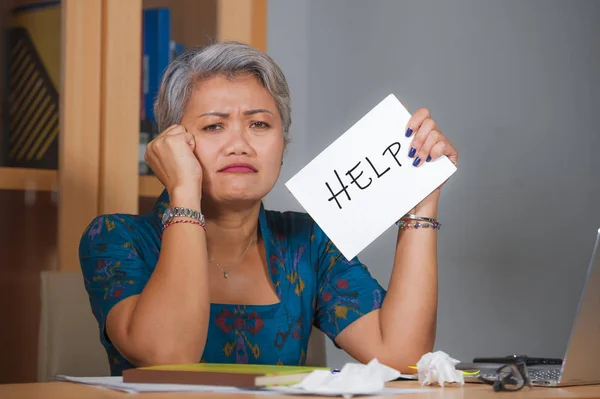 Atractiva mujer asiática estresada y sobrecargada de trabajo que trabaja en el escritorio de la computadora portátil de la oficina en la sensación de estrés frustrado e indefenso pidiendo ayuda sosteniendo el bloc de notas —  Fotos de Stock