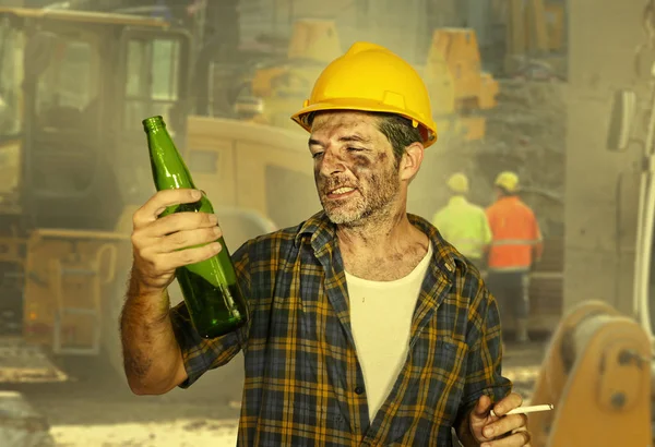 Müder Bauarbeiter oder Bauarbeiter mit Schutzhelm, der sich erschöpft fühlt und während der Arbeitspause auf der Baustelle eine kalte Bierflasche trinkt, lächelt glücklich — Stockfoto