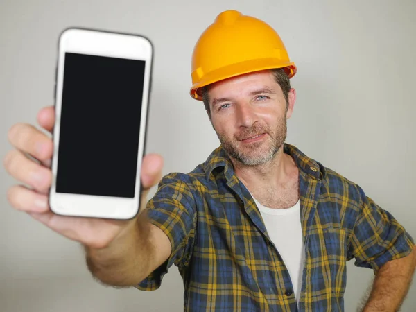 Constructeur werker in aannemer helm houden mobiele telefoon aanbieden van bedrijfsgebouw en reparatiediensten glimlachend vrolijk en zelfverzekerd uitnodigen voor bellen — Stockfoto