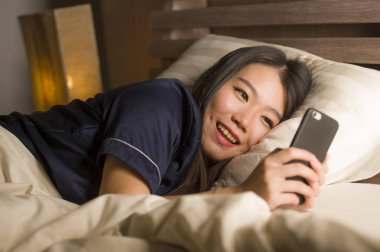 Kız arkadaşı ile cep telefonu sosyal medya manifatura kullanarak pijama genç güzel ve mutlu Asya Çinli kadın veya neşeli gülümseyen online dating app zevk