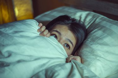 young sleepless beautiful and scared Asian Chinese woman lying on bed awake at night suffering nightmare after watching zombie horror movie in fear and stressed face  clipart