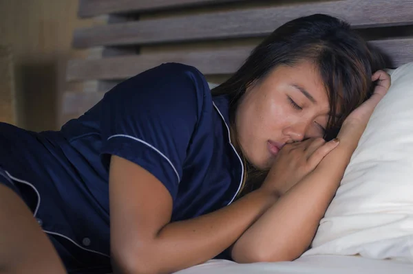 Dramatisches Lifestyleporträt einer jungen attraktiven, traurigen und depressiven Asiatin im Schlafanzug, die unter Schmerzen im Bett liegt und Depressionen und Angstzustände erleidet, die sich einsam und verzweifelt anfühlen — Stockfoto