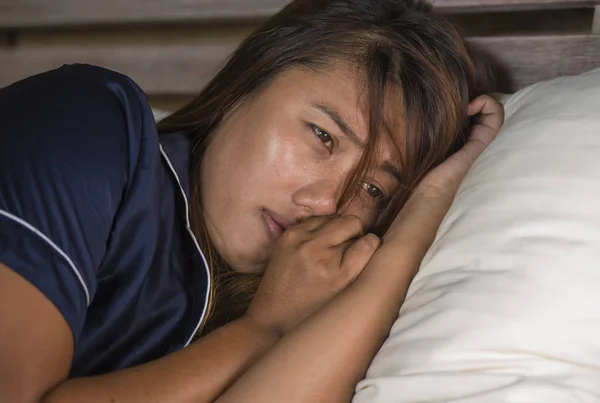 Dramatische Lifestyle portret van jonge aantrekkelijke trieste en depressieve Aziatische vrouw in pyjama liggend in bed in pijn lijden depressie en angst gevoel eenzaam en wanhopig — Stockfoto