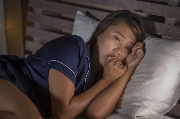 Dramatisches Lifestyleporträt einer jungen attraktiven, traurigen und depressiven Asiatin im Schlafanzug, die unter Schmerzen im Bett liegt und Depressionen und Angstzustände erleidet, die sich einsam und verzweifelt anfühlen — Stockfoto