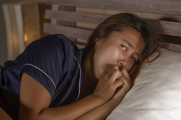 Dramatic lifestyle portrait of young attractive sad and depressed Asian woman in pajamas lying in bed in pain suffering depression and anxiety feeling lonely and desperate — ストック写真