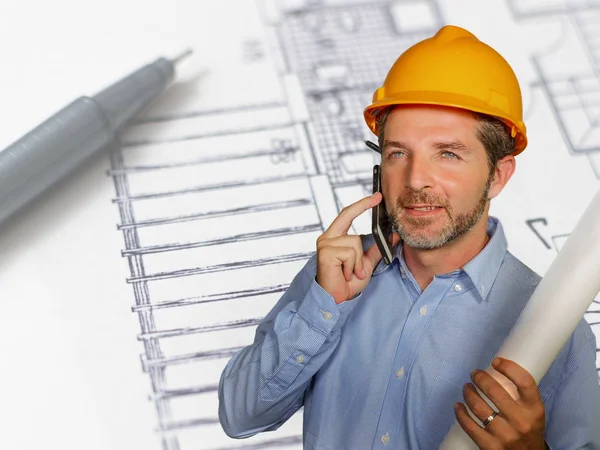 Corporate portret van jonge aantrekkelijke en gelukkig industrieel ingenieur man of architect in veiligheid bouwer helm praten op mobiele telefoon op het opbouwen van project blauwdruk — Stockfoto