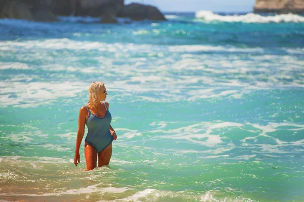 Junge glückliche und sexy blonde Frau in einem Stück Badeanzug im Wasser mit Blick auf das Meer in atemberaubenden schönen tropischen Strand genießen unbeschwerten Sommerurlaub — Stockfoto