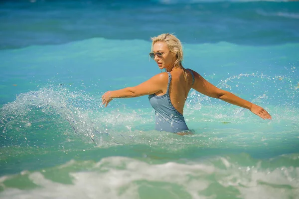 Junge glückliche und sexy blonde Frau im Badeanzug-Bikini spielt mit den Wellen im Meer an einem atemberaubend schönen tropischen Strand und genießt unbeschwerte Sommerferien — Stockfoto