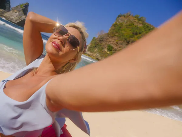 여름 휴가 여행에서 휴대 전화와 아름다운 열대 해변과 함께 휴가 셀카 사진을 찍는 비키니에 젊은 행복하고 매력적인 금발 머리 여자 — 스톡 사진