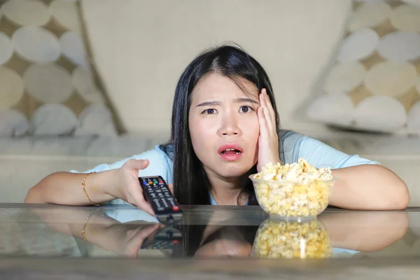 Joven hermosa y relajado asiático japonés mujer viendo coreano drama en televisión en triste romántico película comer palomitas de maíz en casa sala de estar sofá concentrado —  Fotos de Stock