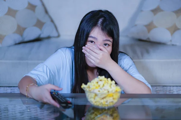 Junge schöne und verängstigte asiatische Teenager Frau in Angst Horrorfilm zu Hause Sofa Sofa essen Popcorn-Schüssel mit Fernbedienung — Stockfoto