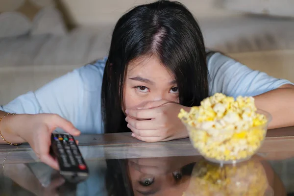 Joven hermosa y asustada asiático coreano adolescente mujer en miedo viendo horror miedo película en casa sofá sofá comer palomitas de maíz bowl holding remote controller — Foto de Stock