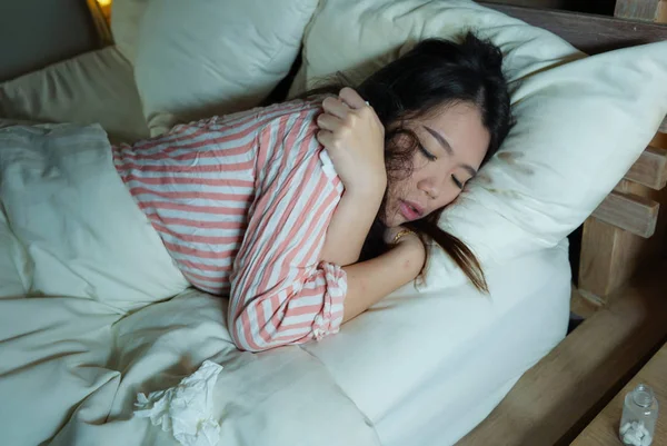 Wanita Cina muda yang lelah dan sakit terbaring sakit di tempat tidur dengan piyama di malam hari dengan kertas tisu menderita dingin dan flu merasa tidak sehat dan lelah dalam konsep perawatan kesehatan — Stok Foto