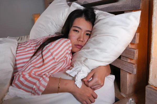 Young beautiful tired and sick Asian Chinese woman lying ill on bed in pajamas at night with tissue papers suffering cold and flu feeling unwell and exhausted in health care concept — Stock Photo, Image