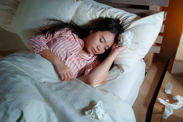 Young beautiful tired and sick Asian Japanese woman lying ill on bed in pajamas at night with tissue papers suffering cold and flu feeling unwell and exhausted in health care — Stock Photo, Image