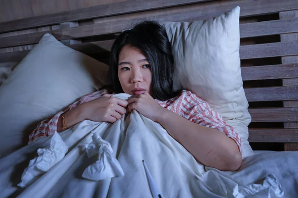 Young beautiful tired and sick Asian Japanese woman lying ill on bed in pajamas at night with tissue papers suffering cold and flu feeling unwell and exhausted in health care — Stock Photo, Image