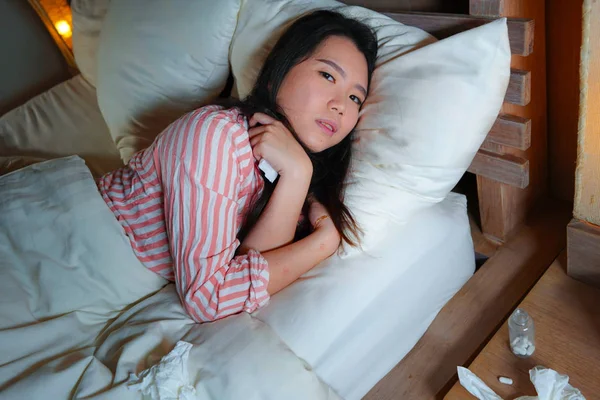 Young beautiful tired and sick Asian Korean woman lying ill on bed in pajamas at night with tissue papers suffering cold and flu feeling unwell and exhausted in health care — Stock Photo, Image