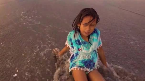 8または9歳の美しく幸せなアジアのインドネシアの子供の女の子のジンバル安定したスローモーションショットは 夏休みを楽しんで水を飛ばす波で遊んで海で遊んでビーチで気楽に遊んでいます — ストック動画
