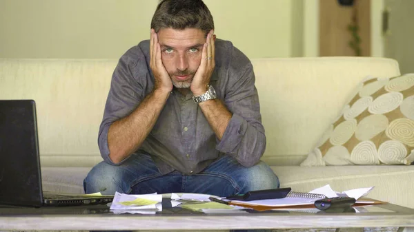 stressed and desperate man at home living room couch doing domestic accounting with paperwork and calculator feeling overwhelmed and worried suffering financial crisis