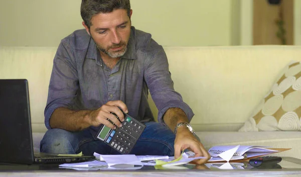 リビングルームのソファソファで若い魅力的で忙しい男性は、国内金融収入と税金をカウント電卓を使用して毎月の費用と借金の支払いを会計 — ストック写真