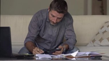genç stresli ve meşgul adam giderleri evrak ve hesap makinesi ile iç muhasebe yapıyor evde oturma odasında kanepede oturan yorgun ve stresli hissediyor ve mali kriz ve para borcu konusunda endişeli yüzünü kapsar 